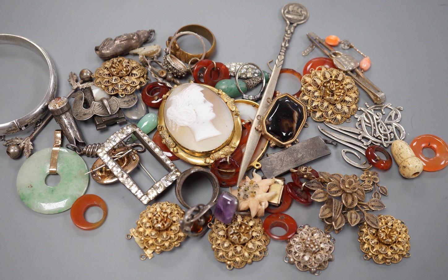 Assorted jewellery including jade pendant, yellow metal buckle brooch, modern silver hinged bangle, cameos, unmounted oval moonstone, agate set white metal buckle brooch, 800 standard paper knife etc.